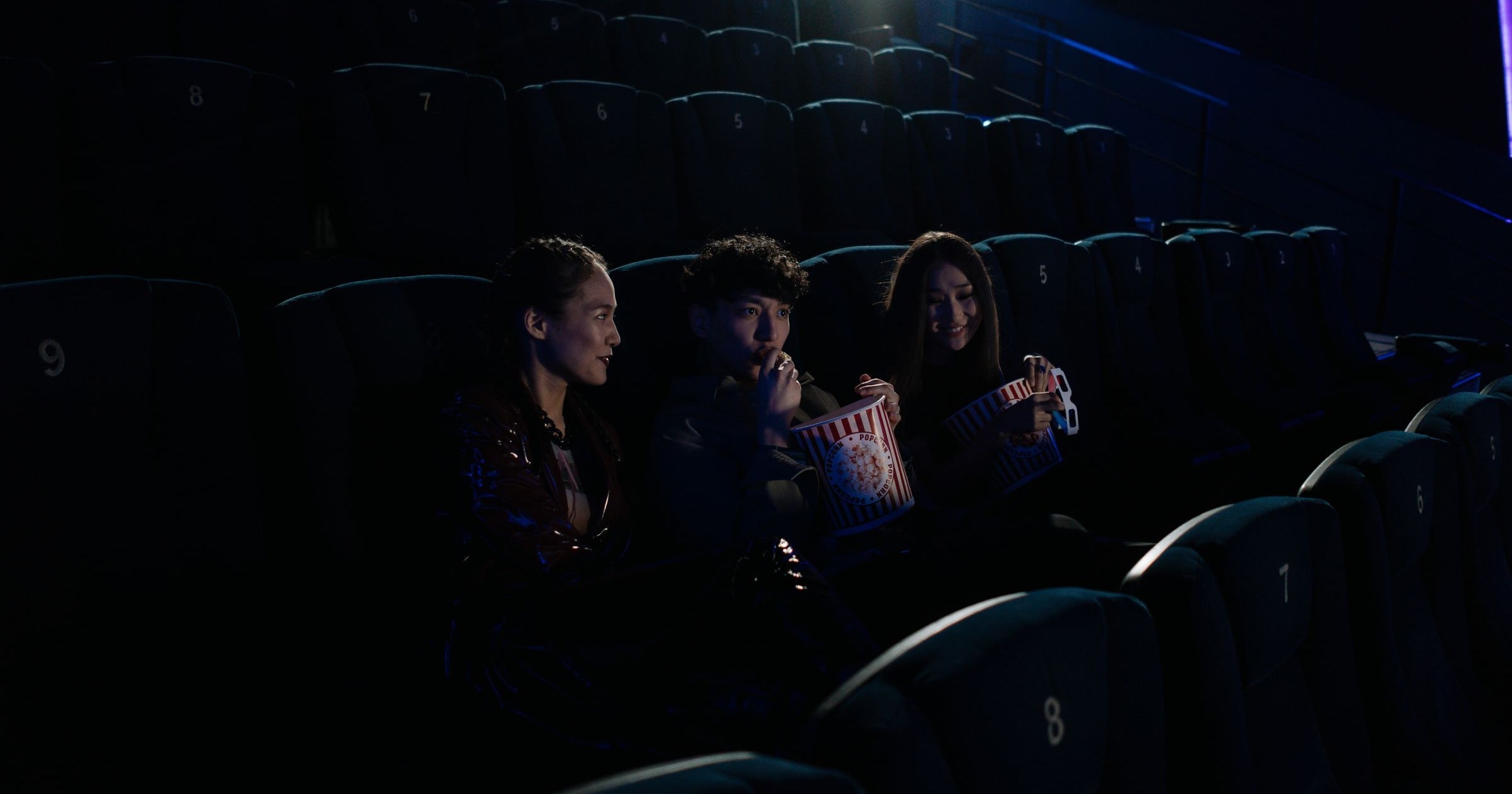 Three people in a darkened cinema watching a film and sharing popcorn