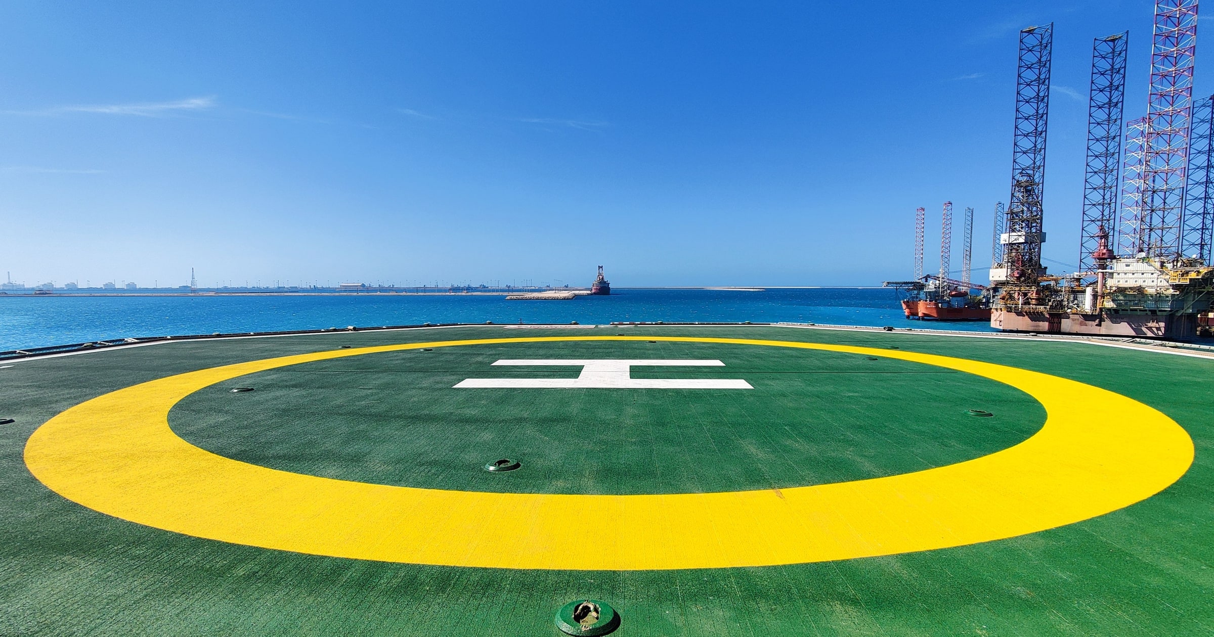 Green and yellow helipad by the water under a clear blue sky, a marked landing zone