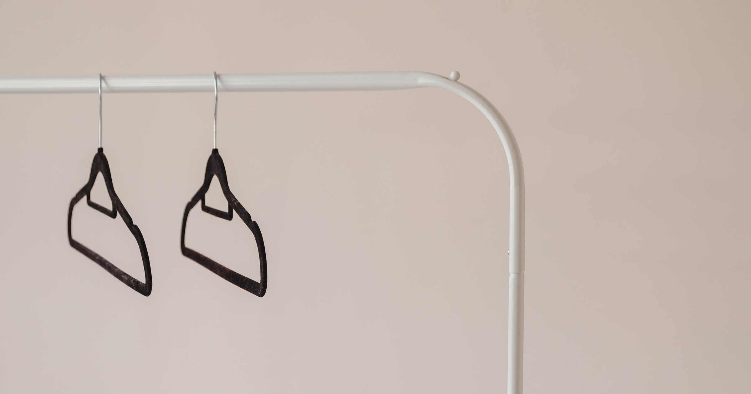 Empty black hangers on a metal clothing rail against a light wall