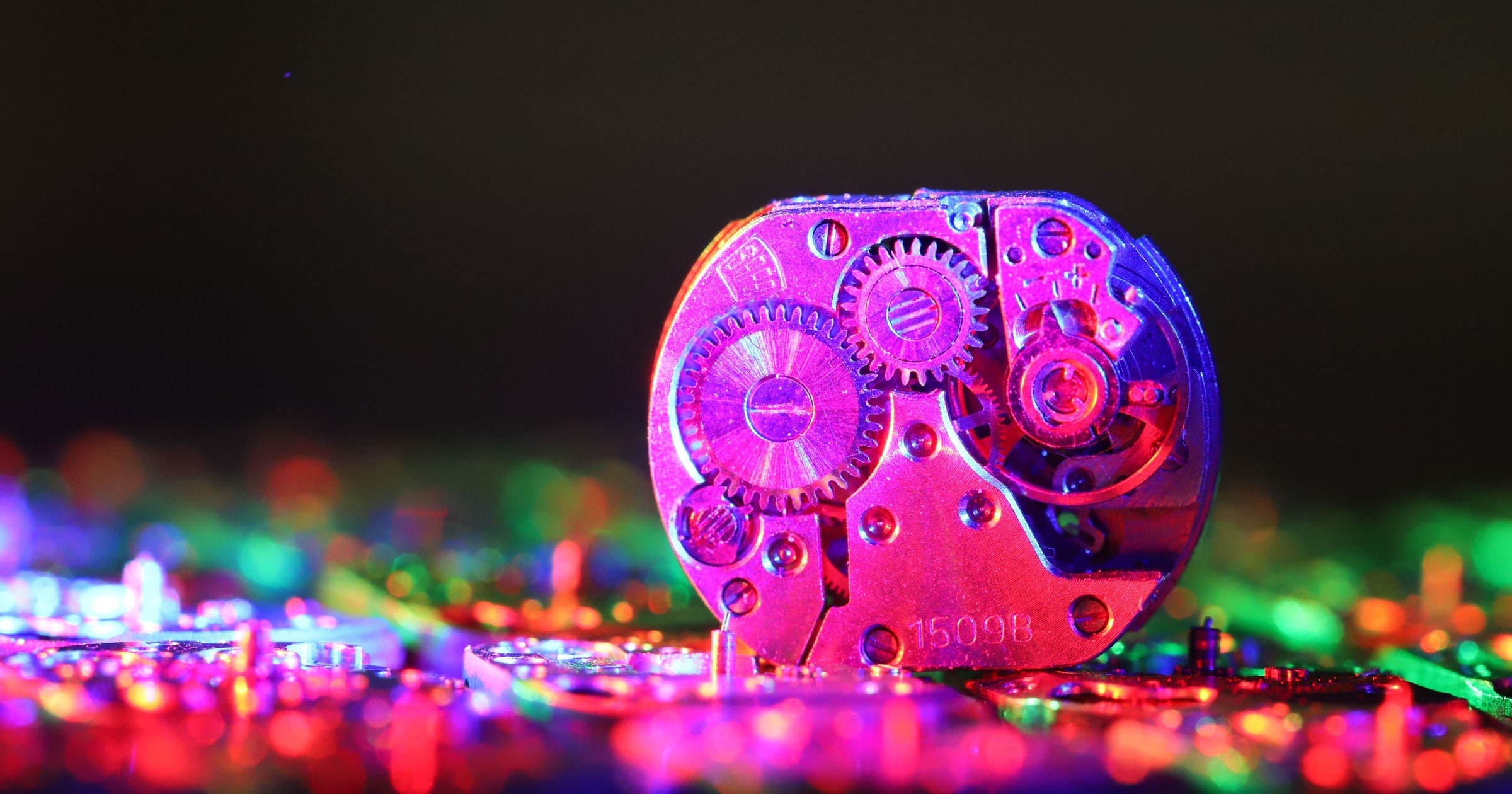 A watch movement standing in a dark room, with other parts blurred behind it