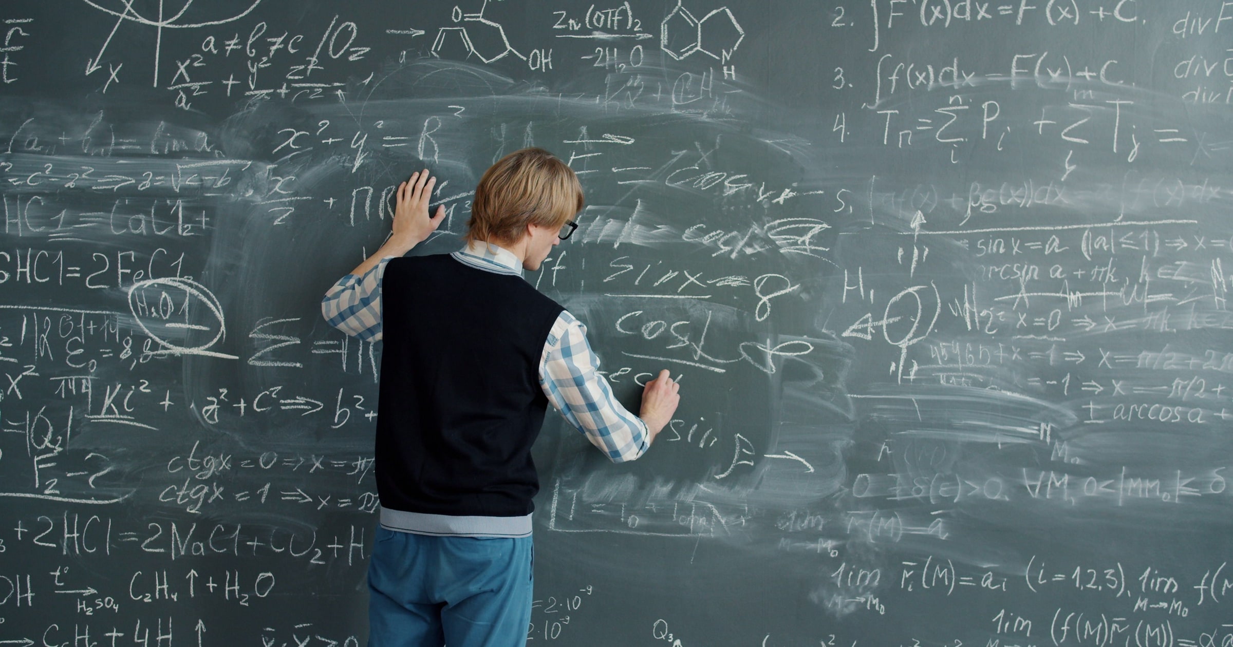 A person writing mathematical formulas on a chalkboard.