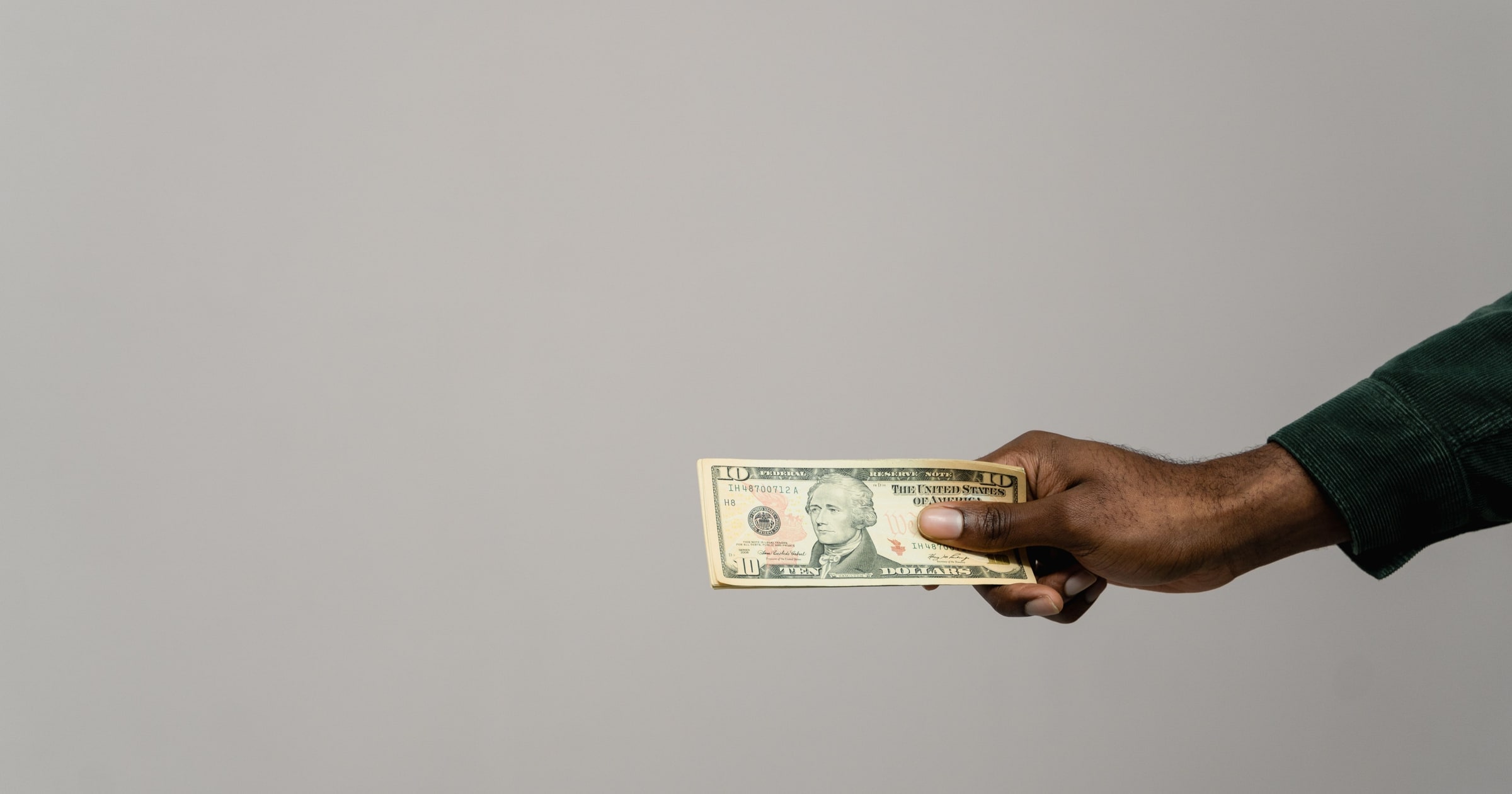 A hand holding a stack of ten-dollar bills